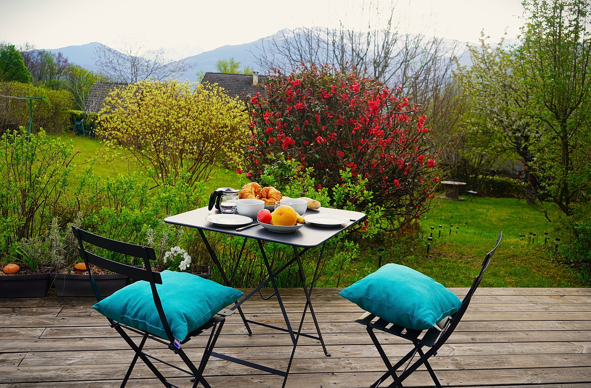 Terrasse du Gîte Vue Blanc — petit-déjeuner face au jardin et aux montagnes, transats bleus et parasol rouge